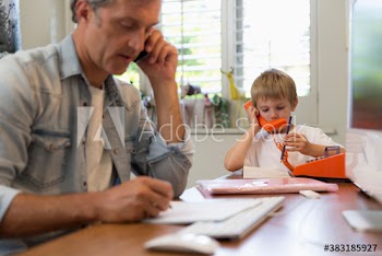 Cute son imitating father on telephone in home office