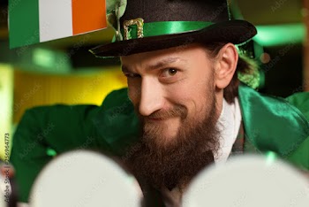 Dark-haired bearded young man in a leprechaun hat looking funny