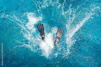 Diver in a wetsuit and flippers jumping in the blue water.
