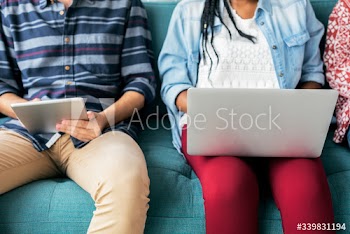 Diverse friends sitting on couch using laptop and tablet