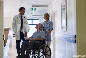 Doctor and nurse talking with senior patient in wheelchair in hospital