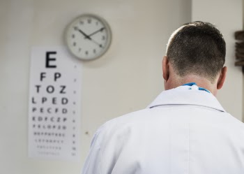 Doctor Facing Snellen Chart Beside Analog Wall Clock Displaying 10:10