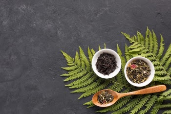 Dried tea herbs in ceramic bowl with fern leaves on black background Free Photo