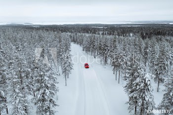 Drone view of a red car driving though a snowy forest in Lapland, Finland