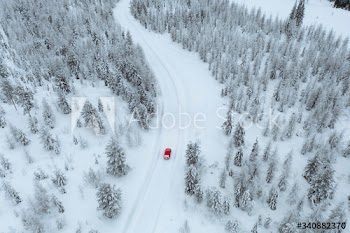Drone view of a red car driving though a snowy forest in Lapland, Finland