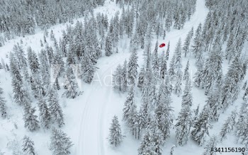 Drone view of a red car driving though a snowy forest in Lapland, Finland