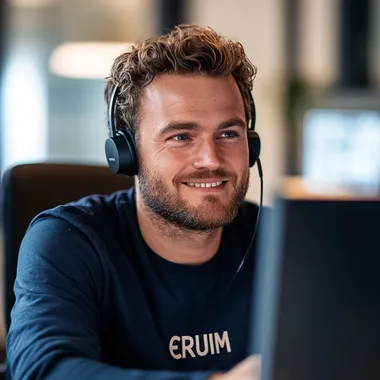 Dutch man in navy office attire using laptop with headset at desk