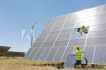 Engineers assembling solar panels in sunny field with wind turbine