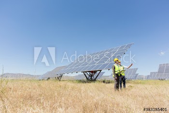 Engineers examining solar panels in sunny field