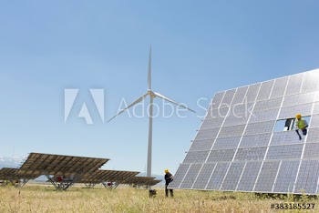 Engineers examining solar panels in sunny field with wind turbine
