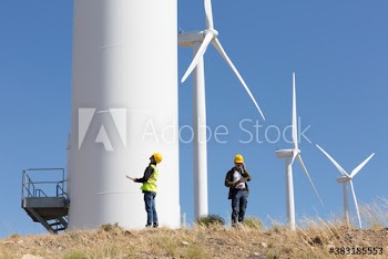 Engineers examining wind turbines on sunny wind farm