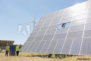 Engineers fixing solar panels in sunny field with wind turbine