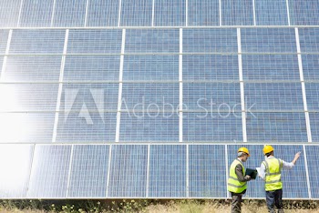 Engineers with laptop meeting below sunny solar panels