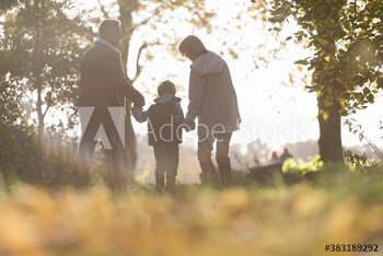Family holding hands and walking in sunny autumn park