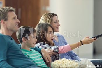 Family watching TV and eating popcorn on sofa