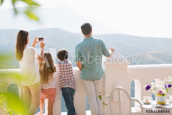Family with camera phone enjoying mountain view from sunny balcony