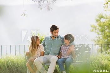 Father and children talking on sunny bench in backyard