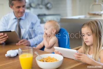 Father and children with digital tablets eating breakfast