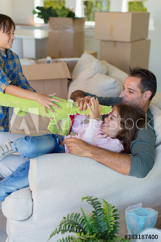 Father and kids playing with stuffed alligator on sofa in new house