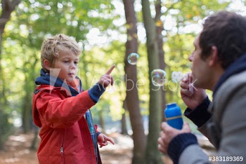 Father and son blowing bubbles in park