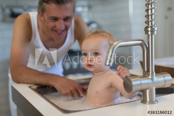 Father bathing baby son in kitchen sink