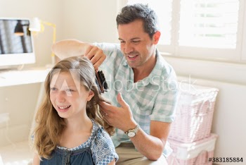 Father brushing hair of daughter in bedroom