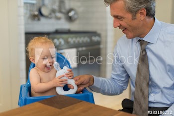 Father giving toy to happy baby son in high chair