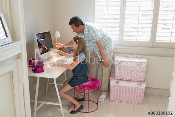 Father helping daughter with computer in bedroom