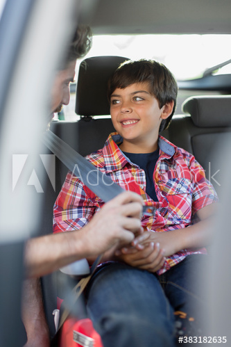 Father helping smiling son with seatbelt inside car
