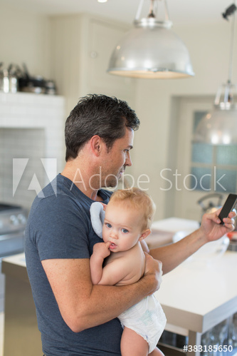 Father holding baby son and using smart phone