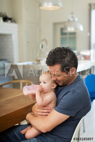 Father holding baby son with baby bottle at dining table
