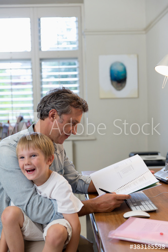 Father holding happy son on lap and working in home office