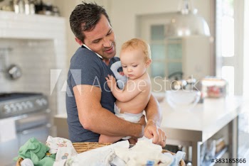 Father multitasking holding baby son and folding laundry