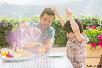 Father pouring orange juice for excited son on sunny patio