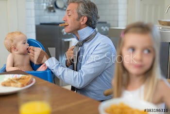 Father preparing for work and feeding baby son in kitchen