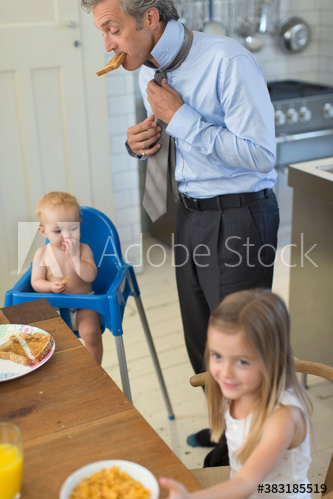 Father preparing for work in kitchen with baby son and daughter
