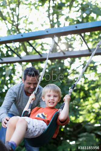 Father pushing son on playground swing