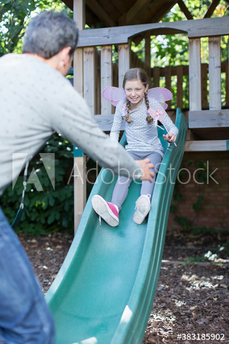 Father reaching for daughter on playground slide
