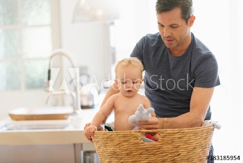 Father showing toy to baby son in laundry basket