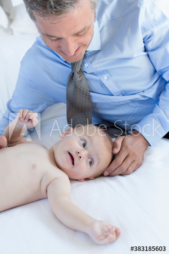 Father watching cute baby son on bed