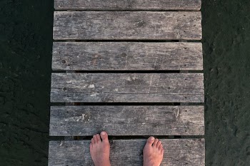 Feet On A Dock Over Rocky Sandy Ground
