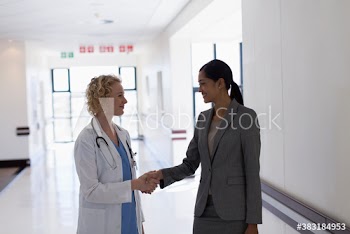 Female doctor and administrator shaking hands in hospital corridor