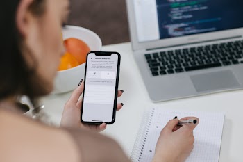 Female holding an iPhone X and taking notes