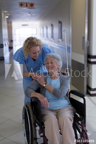 Female nurse comforting senior patient in wheelchair in hospital corridor
