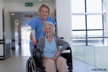 Female nurse pushing senior patient in wheelchair in hospital corridor