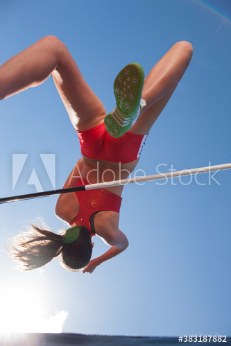 Female track and field athlete high jumping under sunny sky