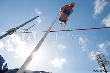 Female track and field athlete pole vaulting under sunny sky
