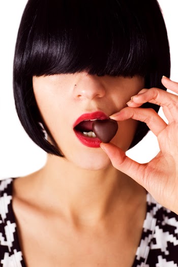 female with bob hairstyle covering her eyes biting a heart shaped chocolate