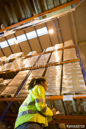 Female worker standing below boxes on shelf in distribution warehouse