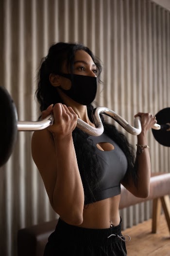 Fit sportswoman in mask exercising with barbell